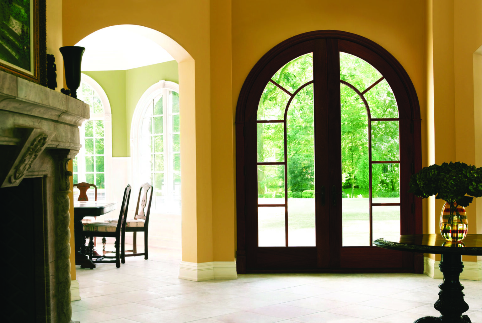 Arched front door shot from the interior of a home, the door has heavy walnut wood and glass paneling