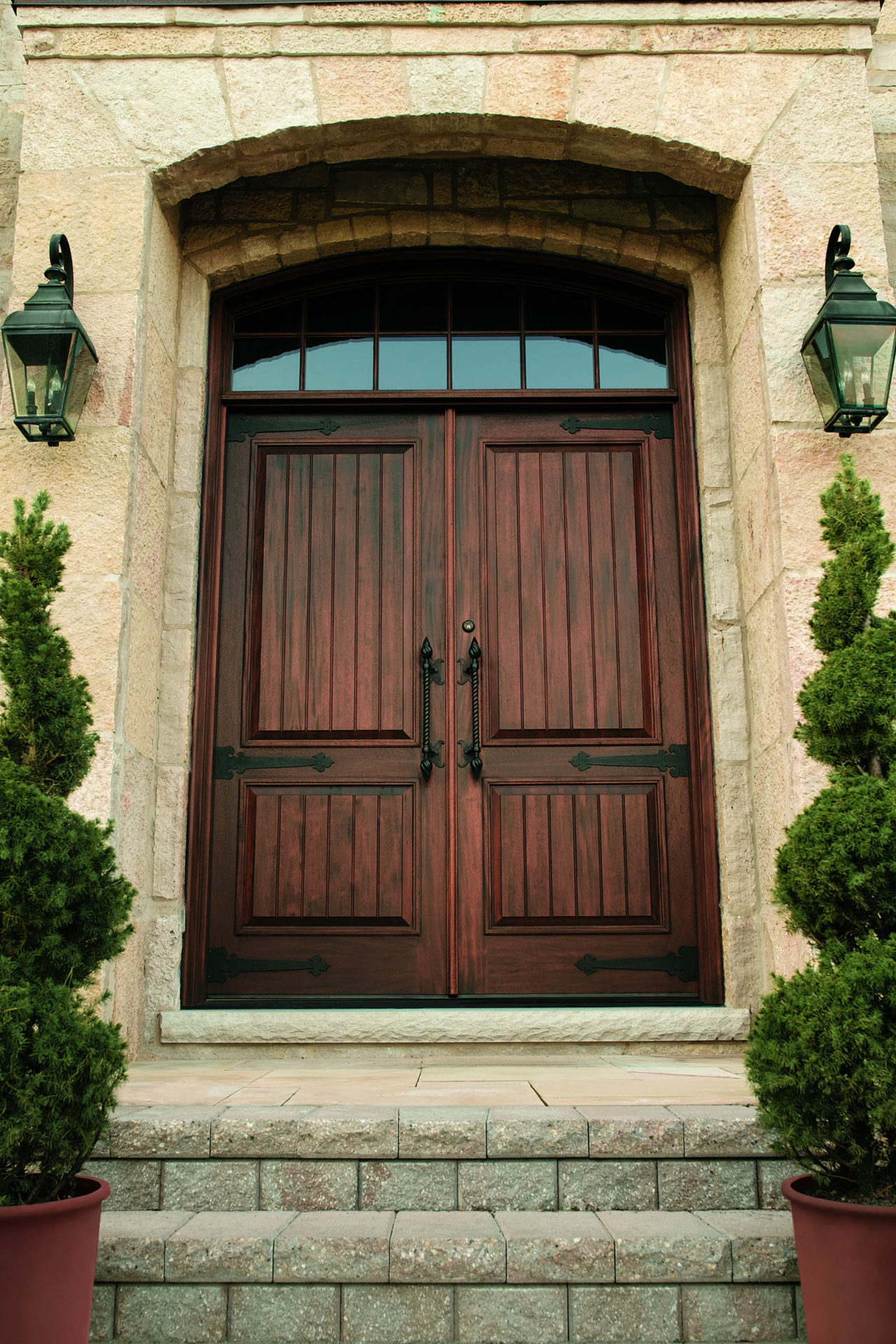 Andersen mahogany front door on a stone house flanked by lanters and shrubs