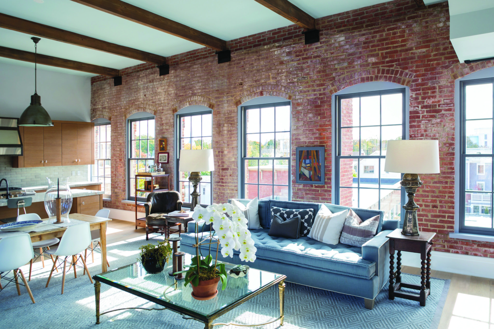 Industrial living room with brick wall, wood beam ceilings, and Andersen E series up and down windows