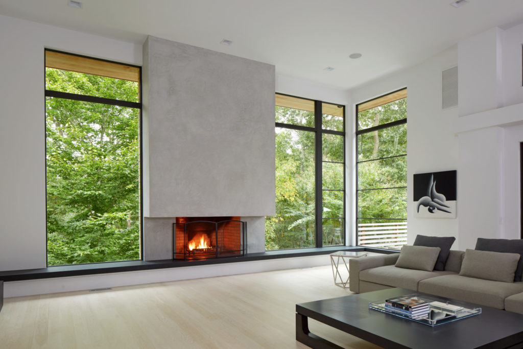 Open concept living room with fireplace and floor to ceiling black windows by Andersen
