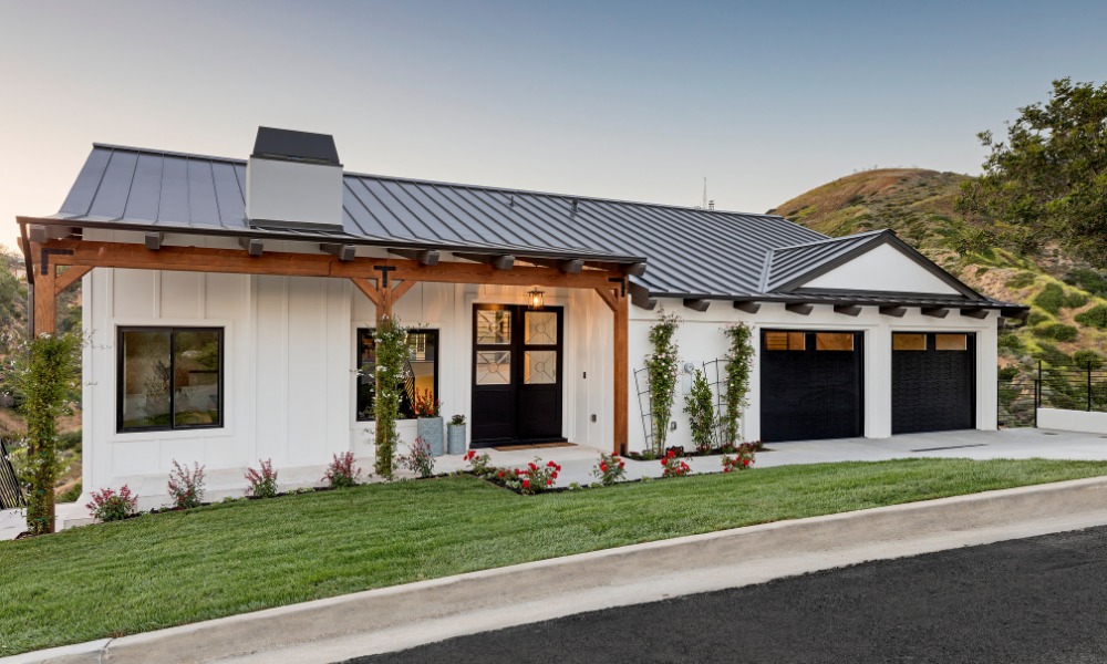 white farmhouse with mental roof, exposed wood porch posts, and black 3/4 light double doors