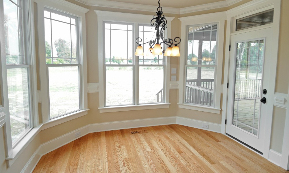 An empty kitchen nook with pine floors, white windows, and a white door to a screened in porch