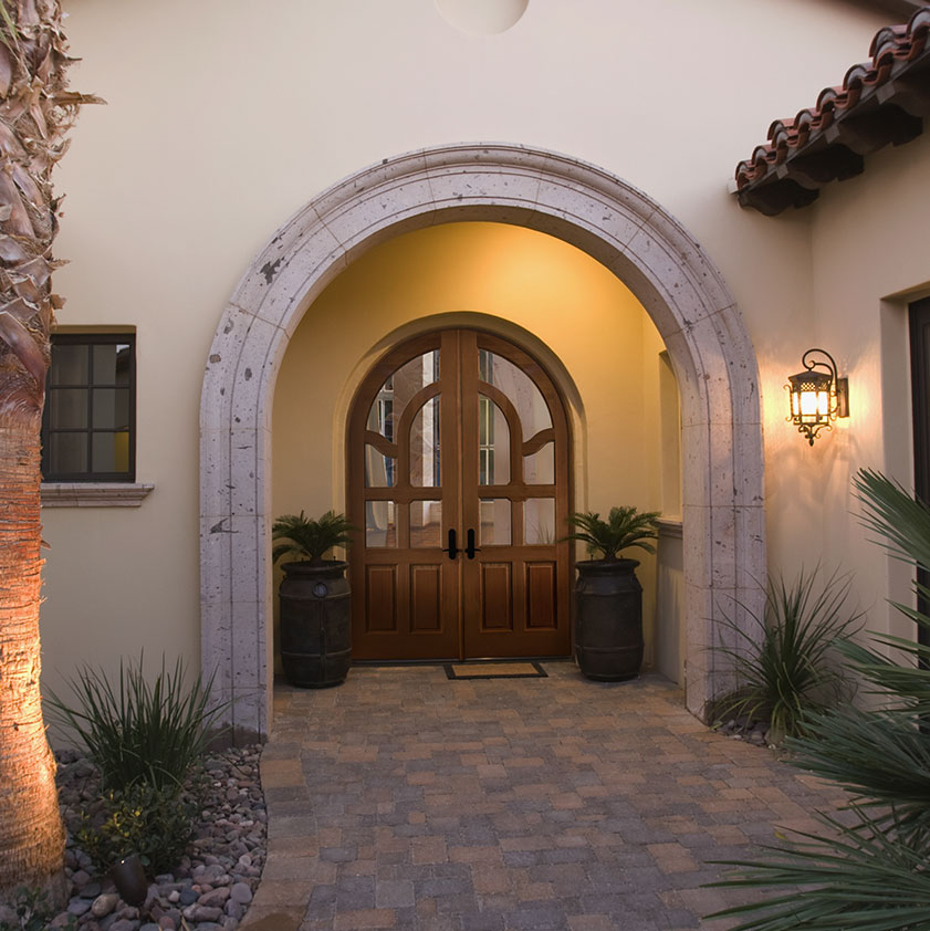 front of a home with a true round-top wood double door, with 3/4 glazing set behind a stone archway with a paver path leading up to it.