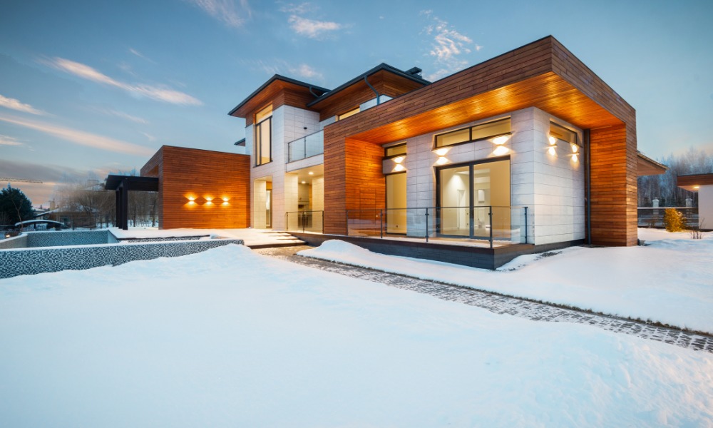 A contemporary home with large black picture windows surrounded by fresh snowfall.