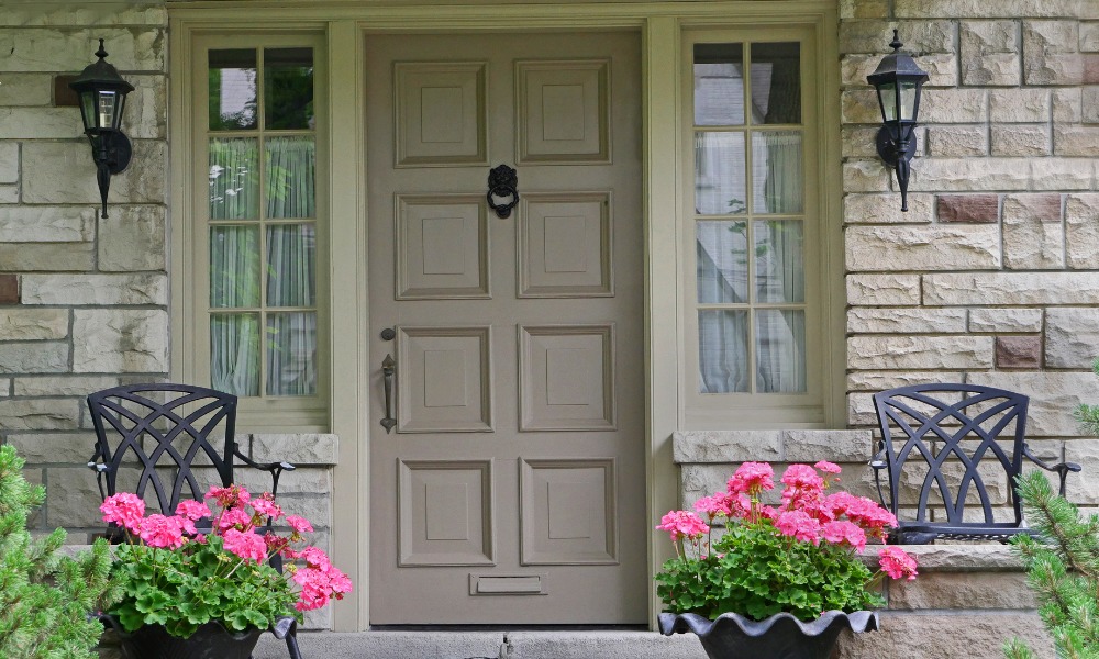 gray wood front door with a wrought iron door knocker, 8-lite sidelites, and pink flowers on the front porch