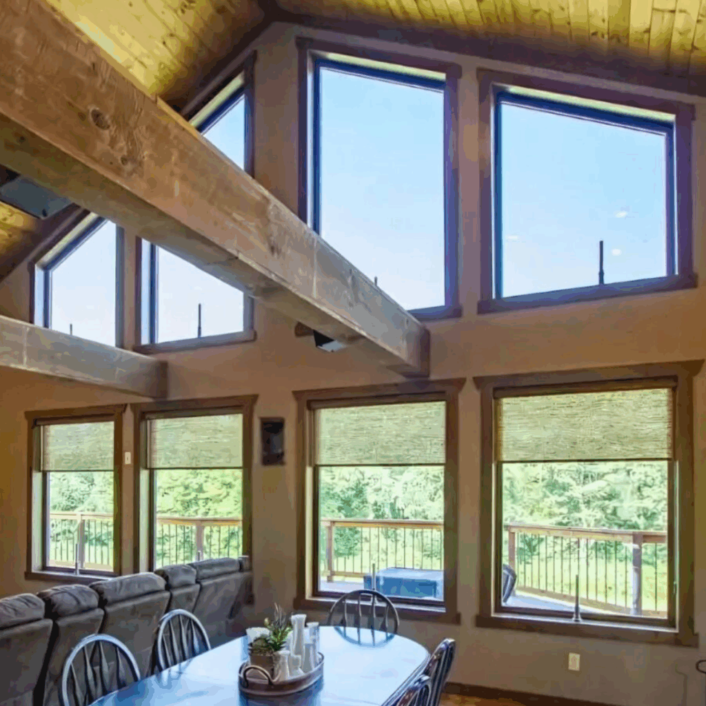 A dining and living area in Apex NC with Andersen Windows, wooden beams, and a vaulted ceiling, allowing ample natural light and views of greenery outside—perfect for homeowners who value style and comfort.