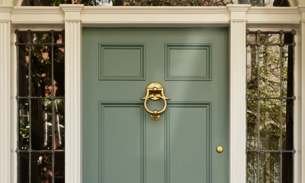 A earthy green front door with a large brass door knocker, flanked by white trim and columns.