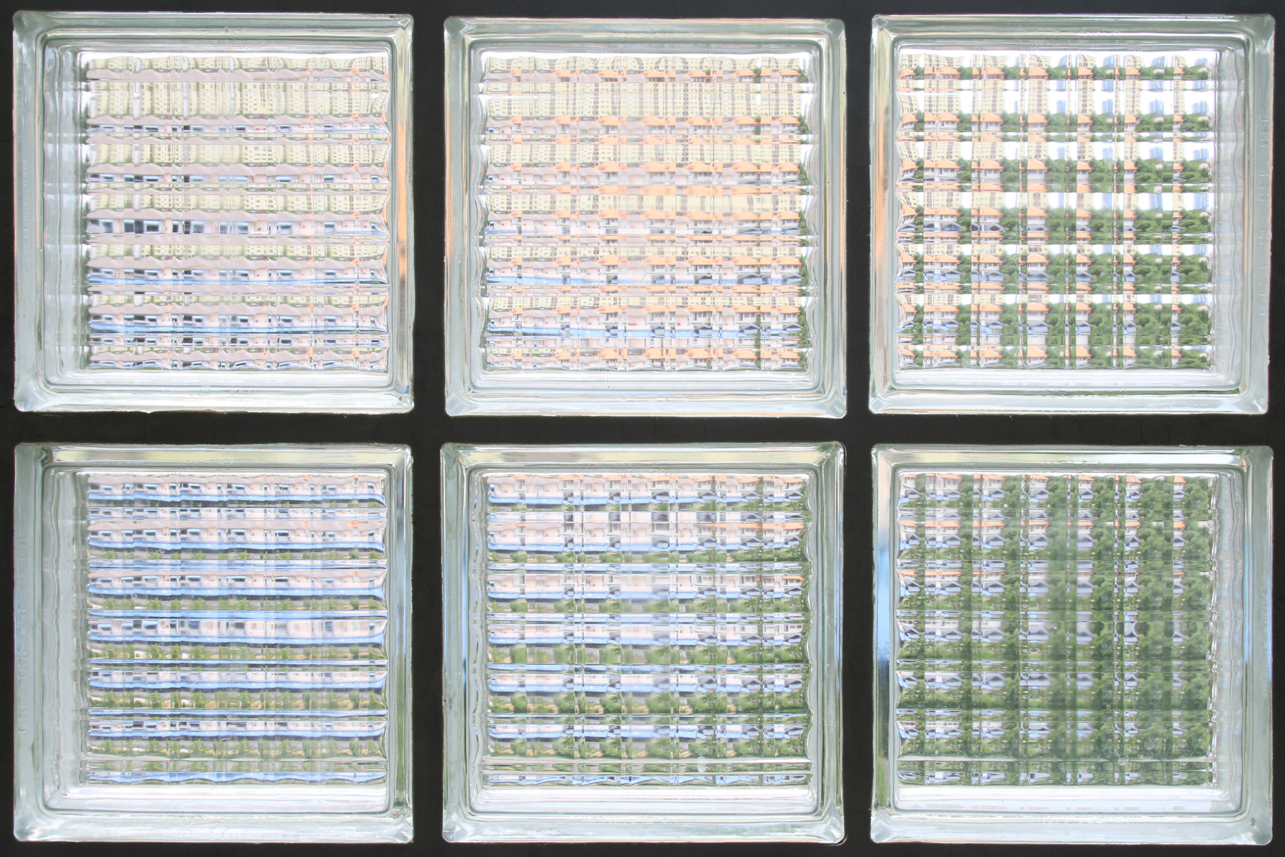 Six square Modern Glass Block Windows are arranged in two rows of three. Each block features a textured, patterned surface, distorting the view of the colors and shapes behind them in hues of green, pink, and white.