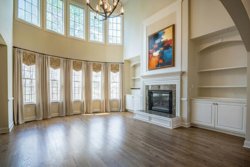 Bright, spacious living room with tall windows—what is a clerestory window in a house but just this—wood floors, high ceiling, chandelier, fireplace with modern art above, built-in shelves, and cream curtains. Natural light fills the elegant space.