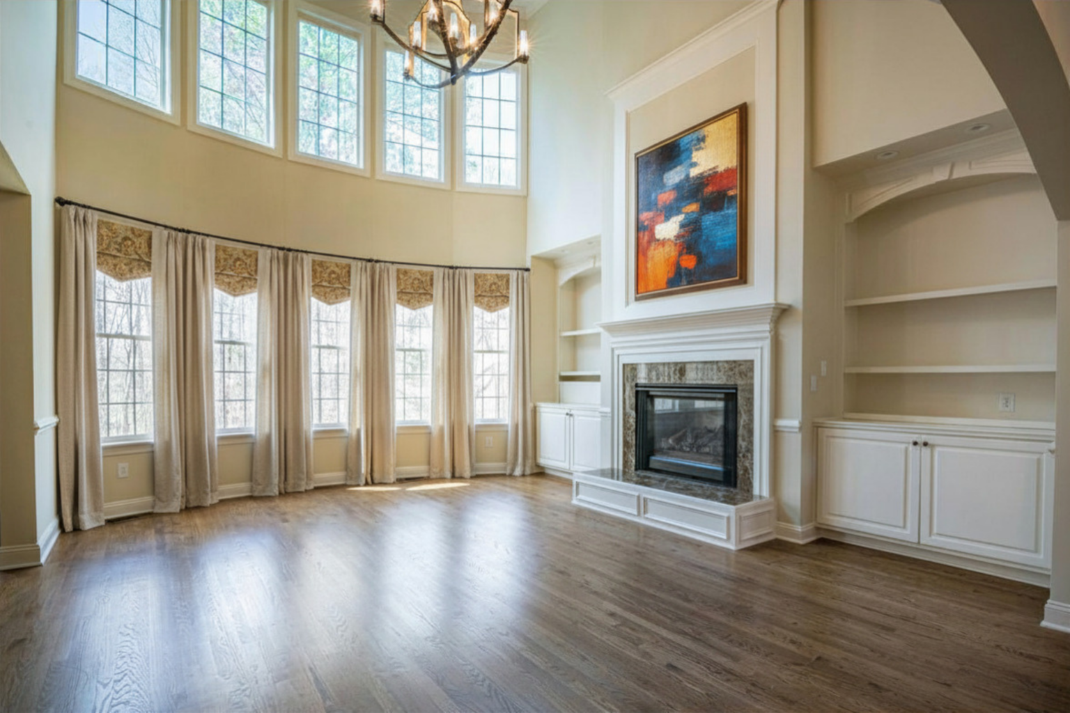 Bright, spacious living room with tall windows—what is a clerestory window in a house but just this—wood floors, high ceiling, chandelier, fireplace with modern art above, built-in shelves, and cream curtains. Natural light fills the elegant space.