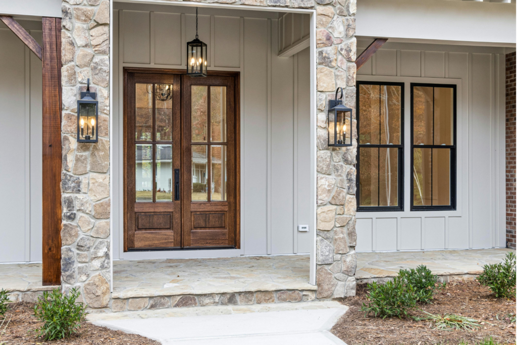 Front exterior view of a house with a stone facade, large black-framed windows, two black lantern lights, and a covered porch with stone flooring—can you replace front door and sidelights with double doors featuring glass panels?.