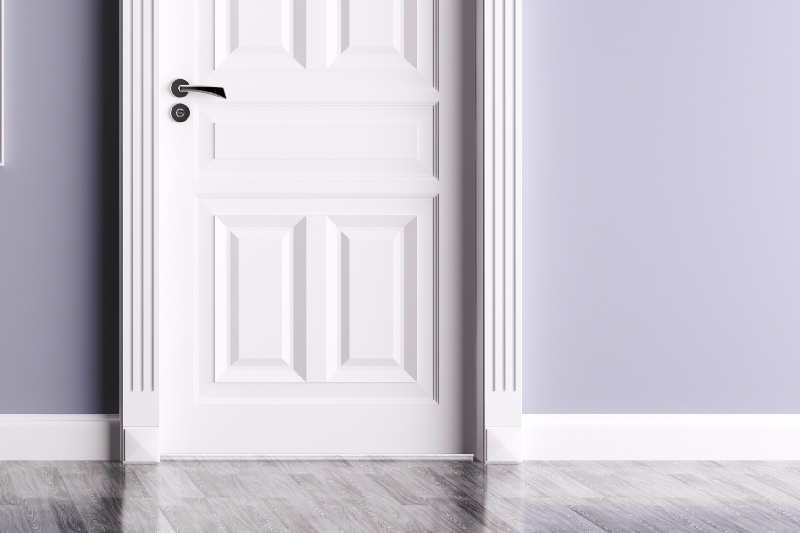 A white, paneled door with a black handle is set in a lavender-colored wall with decorative trim and a plinth block—what is a plinth block on a door? It’s the base piece adding style where trim meets the floor's reflective gray wood planks.