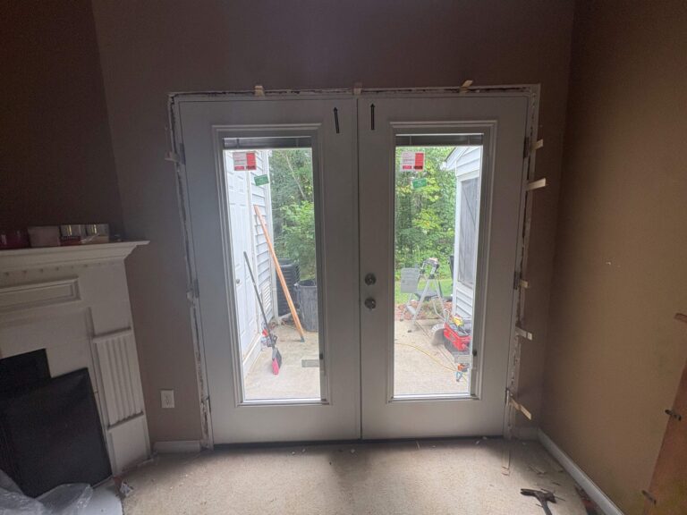 A set of white double doors is installed within a tan-walled interior, with wooden shims exposed along the door frame edges.
